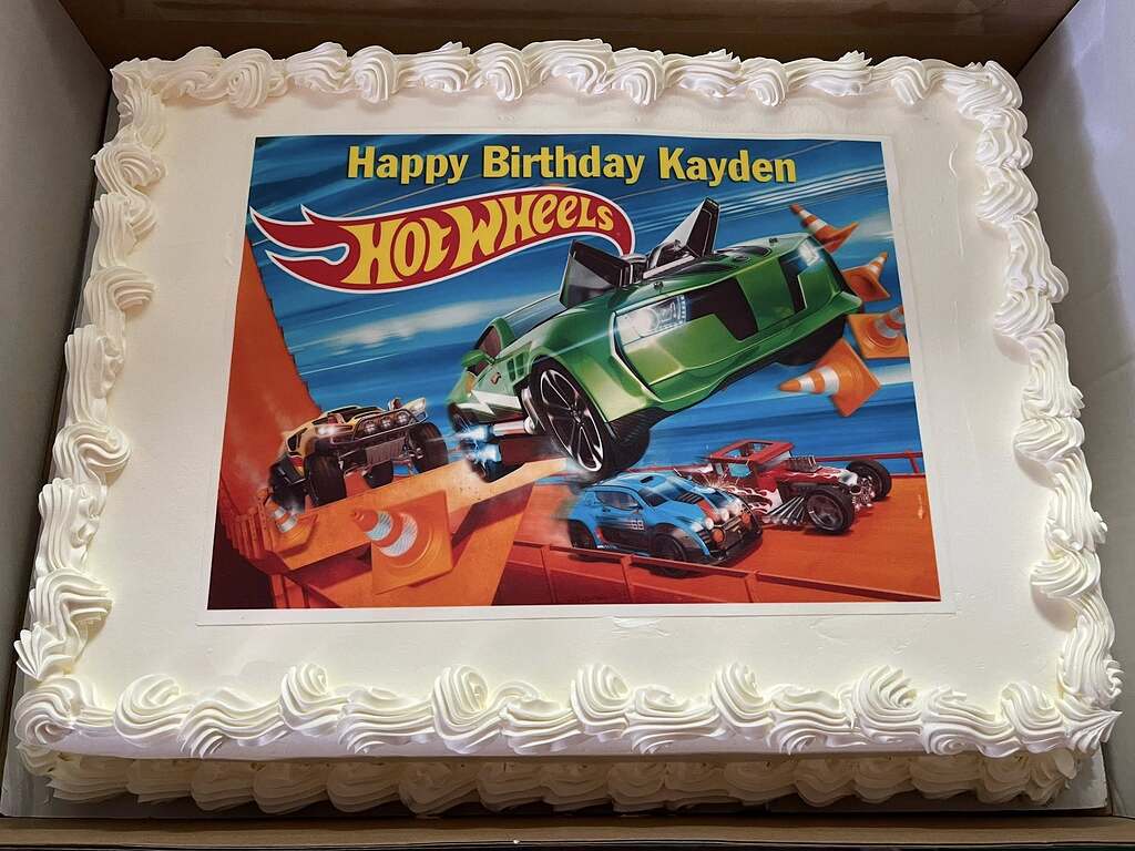 Rectangular sheet cake with white frosting and an edible Hot Wheels birthday topper for Kayden.