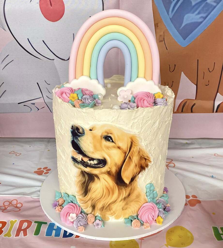 Birthday cake decorated with a Golden Retriever portrait topped with a pastel rainbow and frosting flowers.