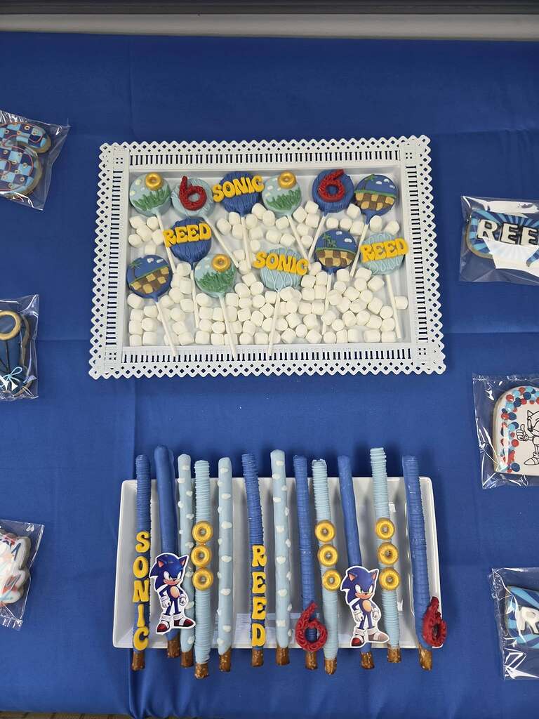 Table display of Sonic the Hedgehog themed birthday treats including decorated cookie pops and chocolate pretzels