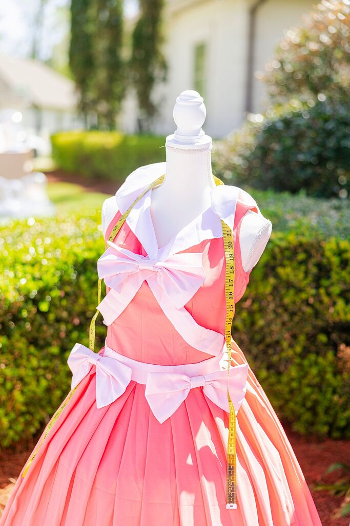 Vintage-style coral pink dress with white collars and decorative bows on dressmaker's mannequin