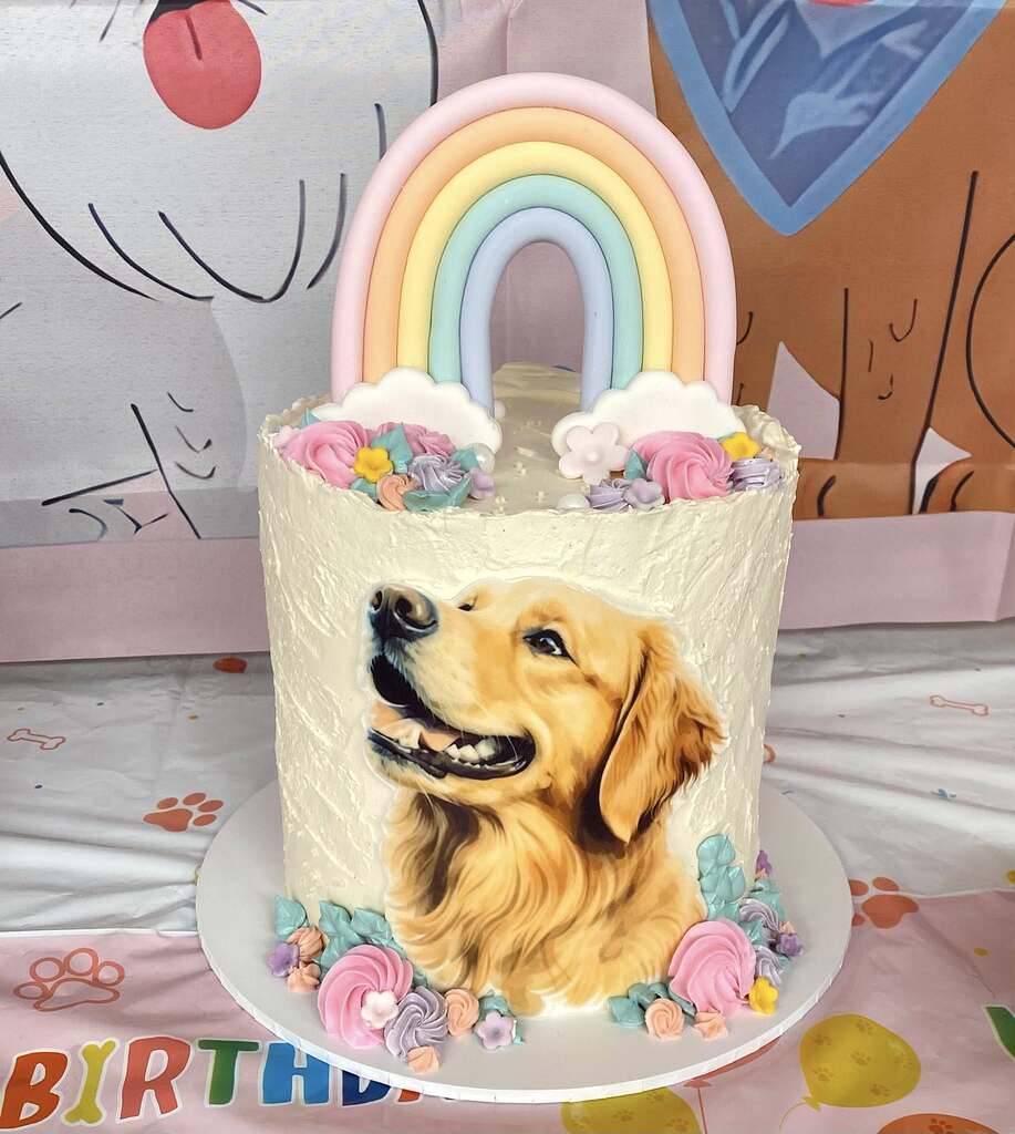 Custom birthday cake featuring a golden retriever portrait, topped with a fondant rainbow and floral decorations.