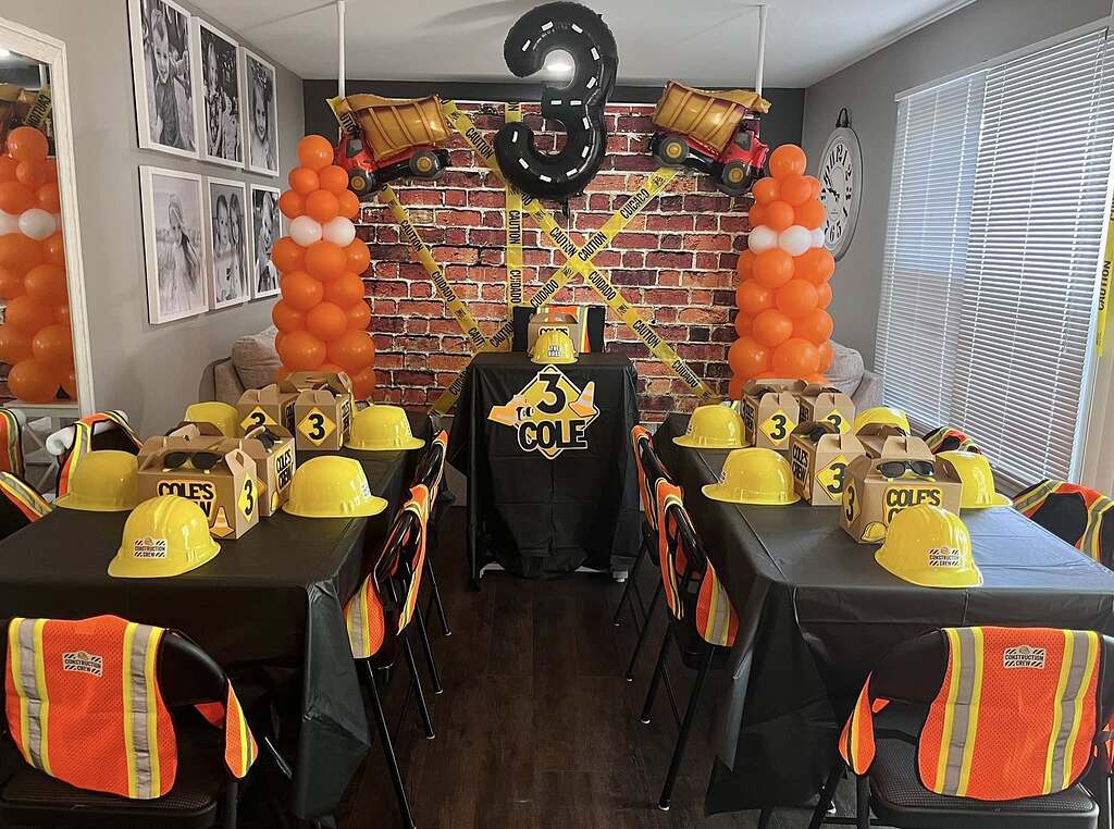 Construction-themed birthday party setup with yellow hard hats, reflective vests, and caution tape decor.