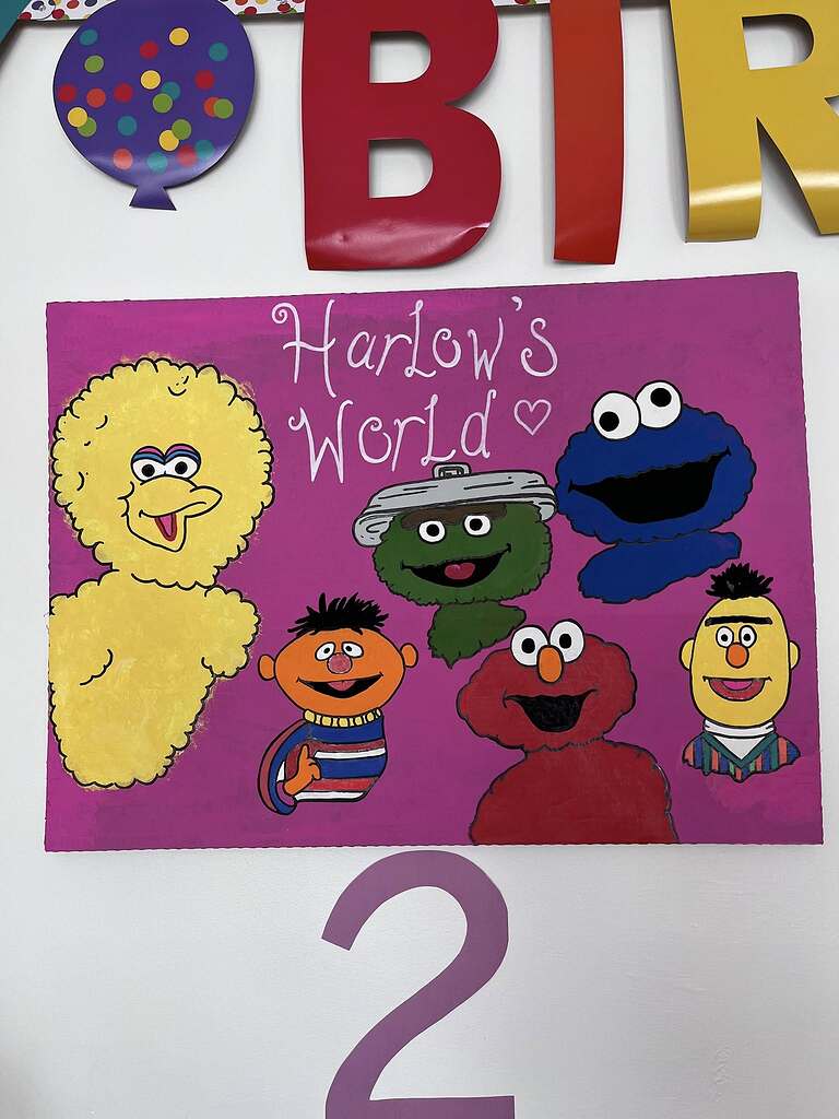 Hand-painted sign on pink background featuring Big Bird, Ernie, Oscar the Grouch, Cookie Monster, Elmo, and Bert with the text Harlow's World.