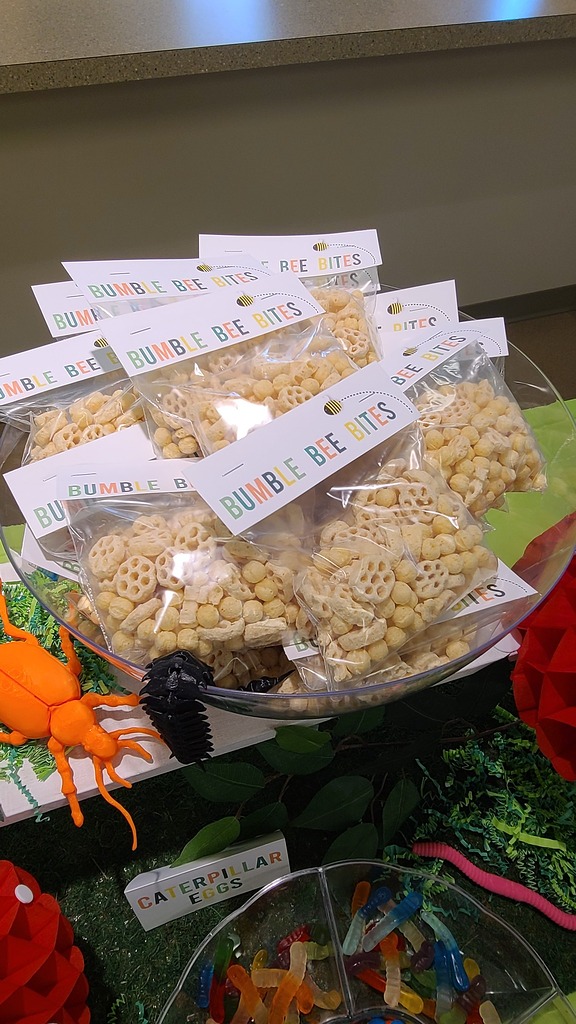 Clear plastic bowls filled with small bags of Bumble Bee Bites snack cereal and a bowl of gummy worms labeled Caterpillar Eggs.