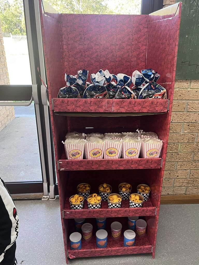 Display rack filled with Disney Cars themed party favor bags, popcorn boxes, snack cups, and Rust-eze themed drink cans.