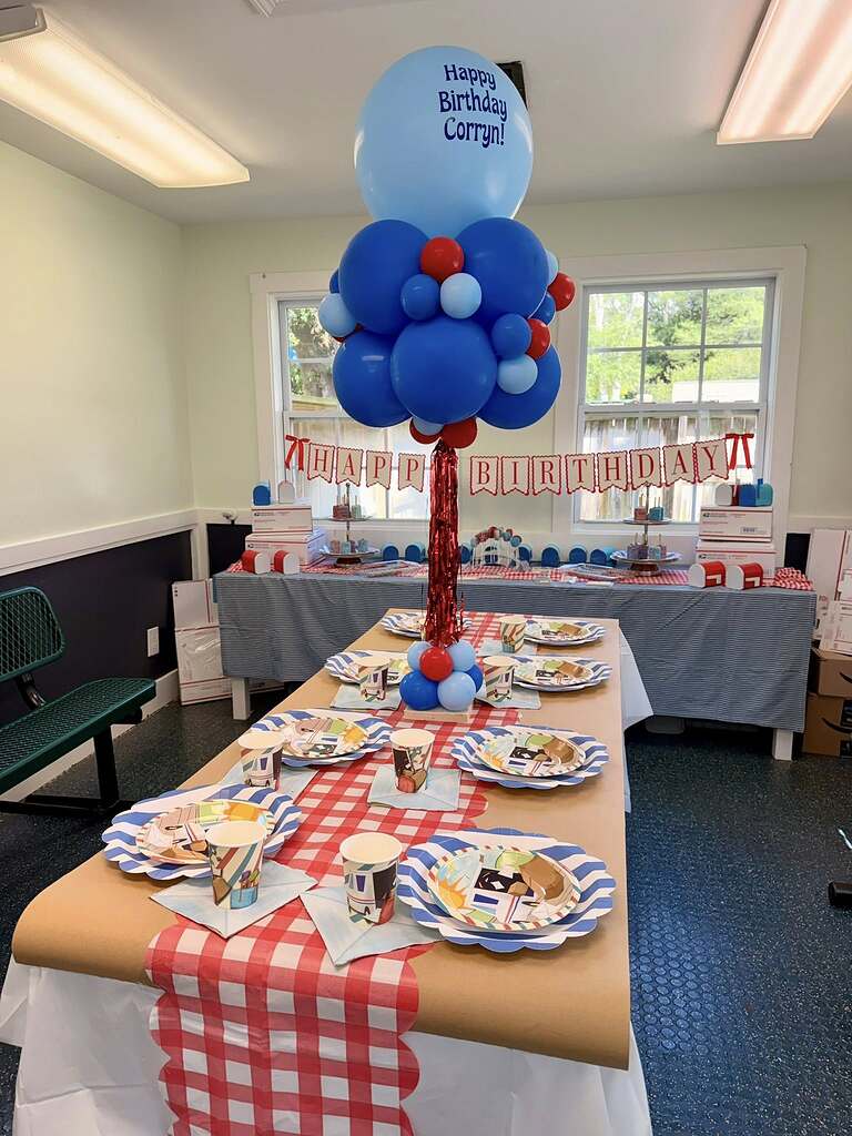 Birthday party table set for USPS-themed celebration with mail carrier plates, cups, and custom balloon centerpiece.