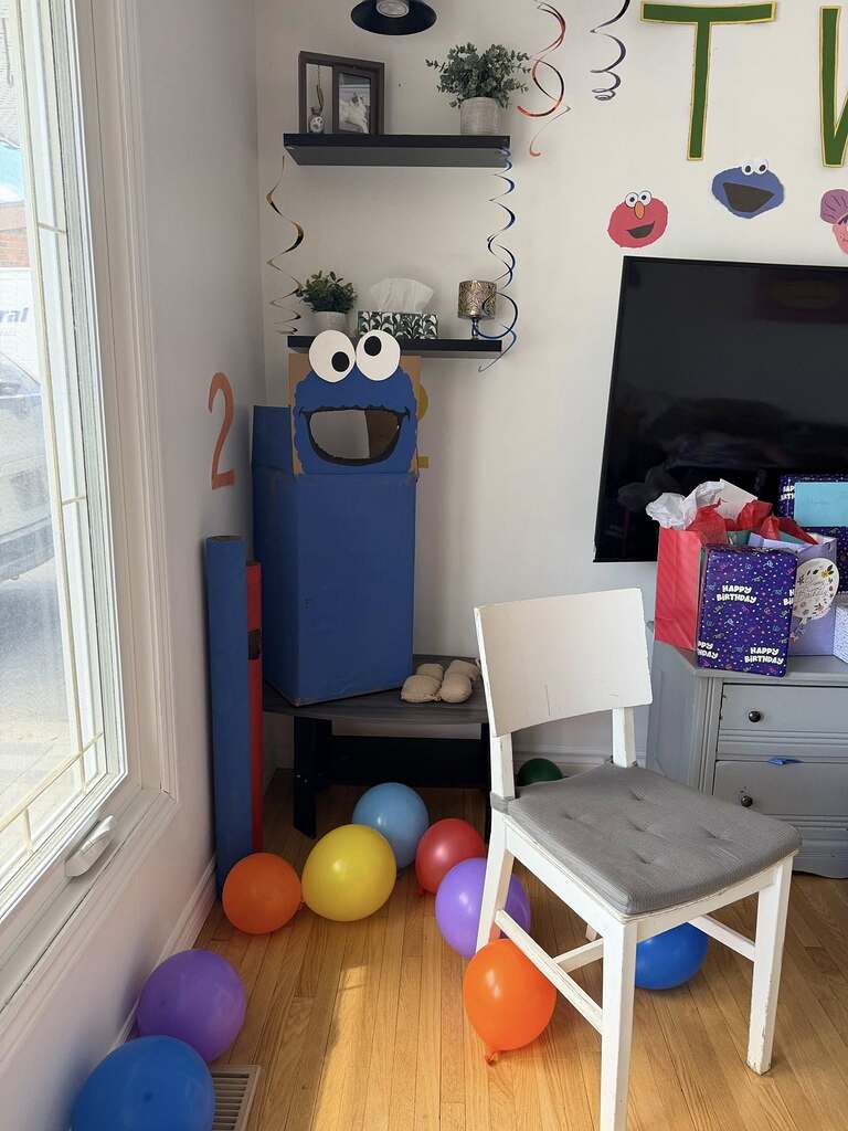 DIY Cookie Monster cardboard cutout used as a prop for a second birthday party filled with colorful balloons.