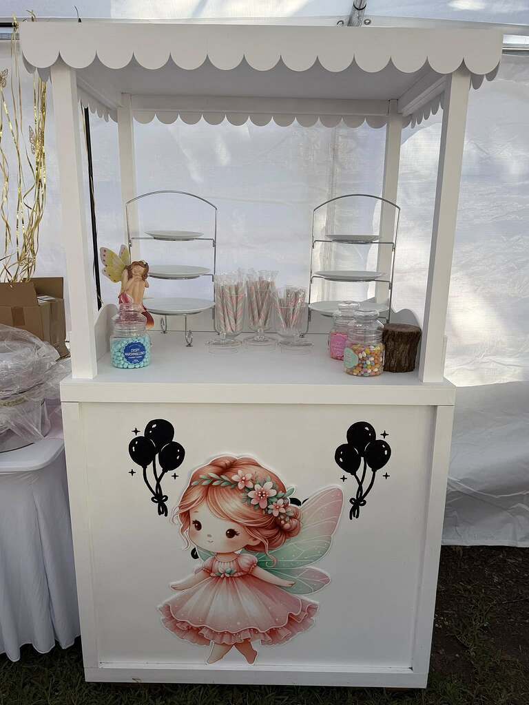 White party snack cart decorated with a fairy illustration and filled with tiers of sweets and candy jars.