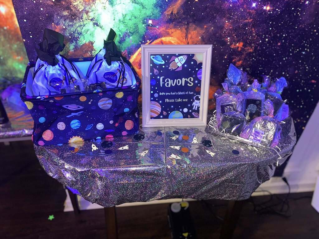 Space themed party favor table with gift bags and a sign that reads Favors, Hope you had a blast of fun, Please take one.