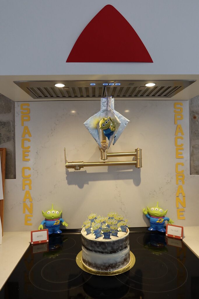 Toy Story Space Crane party display featuring a small alien toy in a hanging claw and a cake topped with aliens.