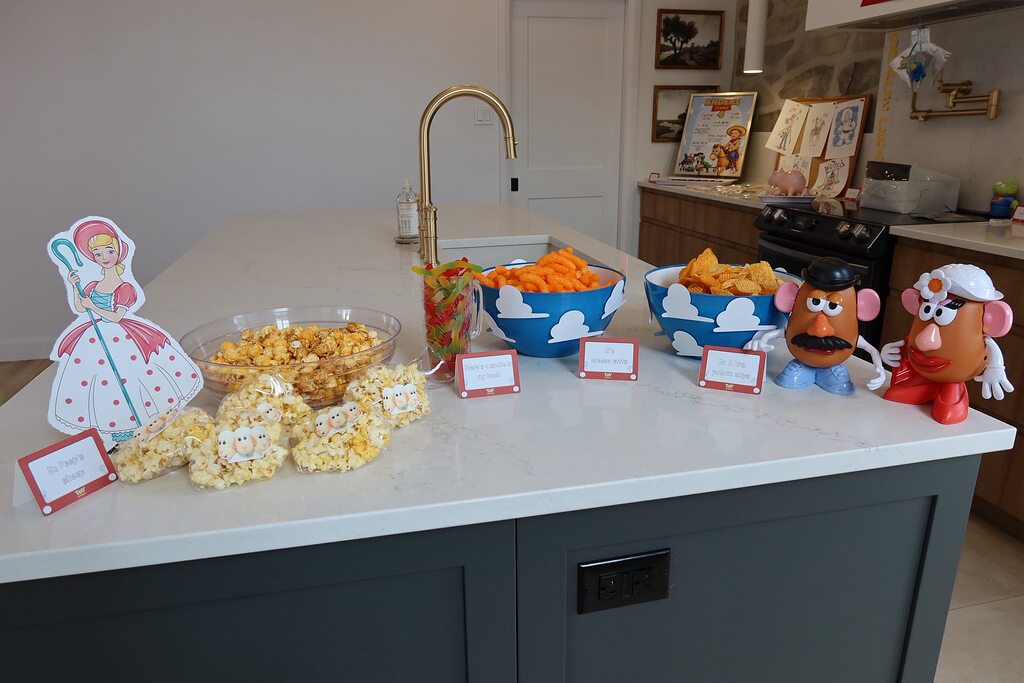 Toy Story themed party snack table featuring character cutouts, bowls of snacks, and Mr. and Mrs. Potato Head figures.