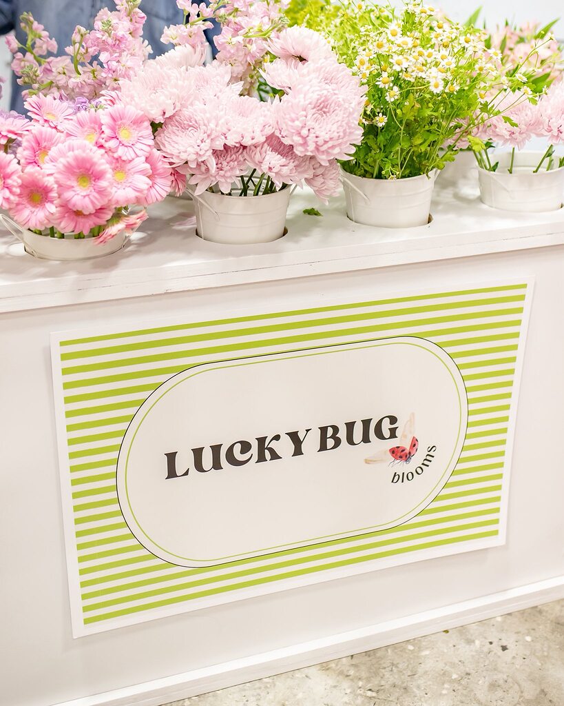 Lucky Bug Blooms branded flower stand with pink gerbera daisies and white flower arrangements in small white buckets