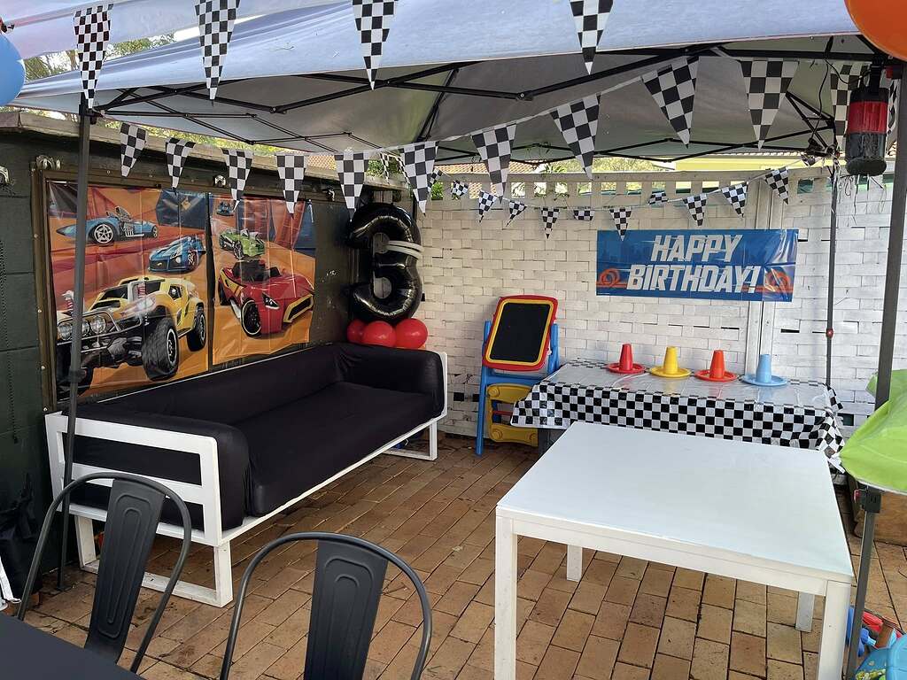Race car themed party setup with checkered flags, a number three balloon, and birthday decorations under a canopy.