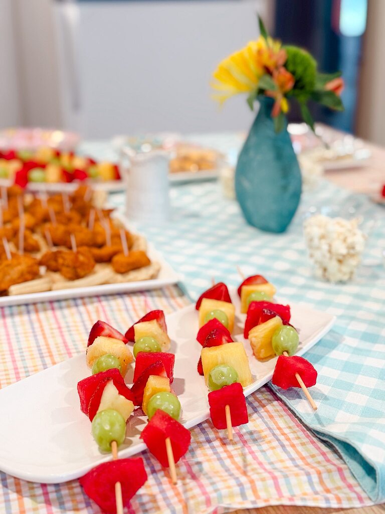 Row of fruit skewers with pineapple, strawberry, watermelon, and grapes on a white plate.