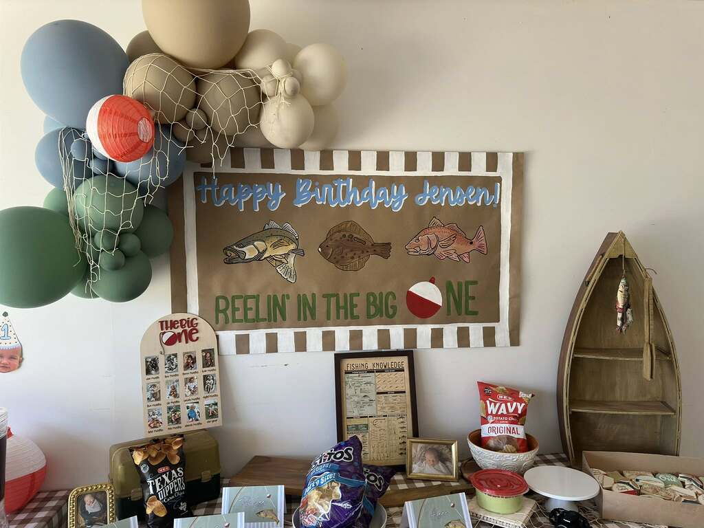 Fishing-themed first birthday party display with personalized banner, balloons, and snacks.