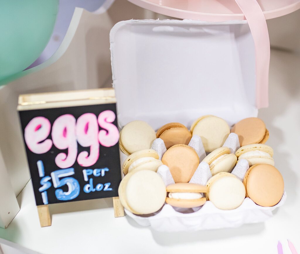 A carton of assorted neutral-toned macarons labeled as eggs for 5 dollars per dozen.
