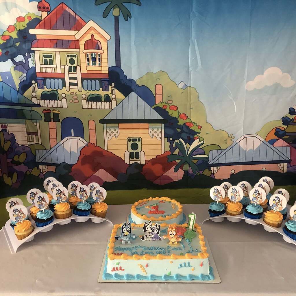 Bluey-themed birthday cake and cupcakes arranged in front of a Heeler house backdrop.