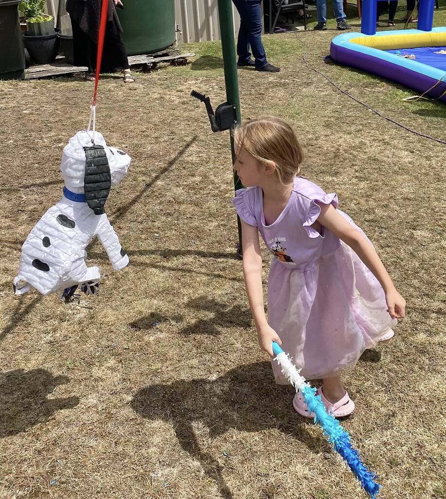 Young girl in a purple dress hitting a Dalmatian-shaped dog pinata at an outdoor party
