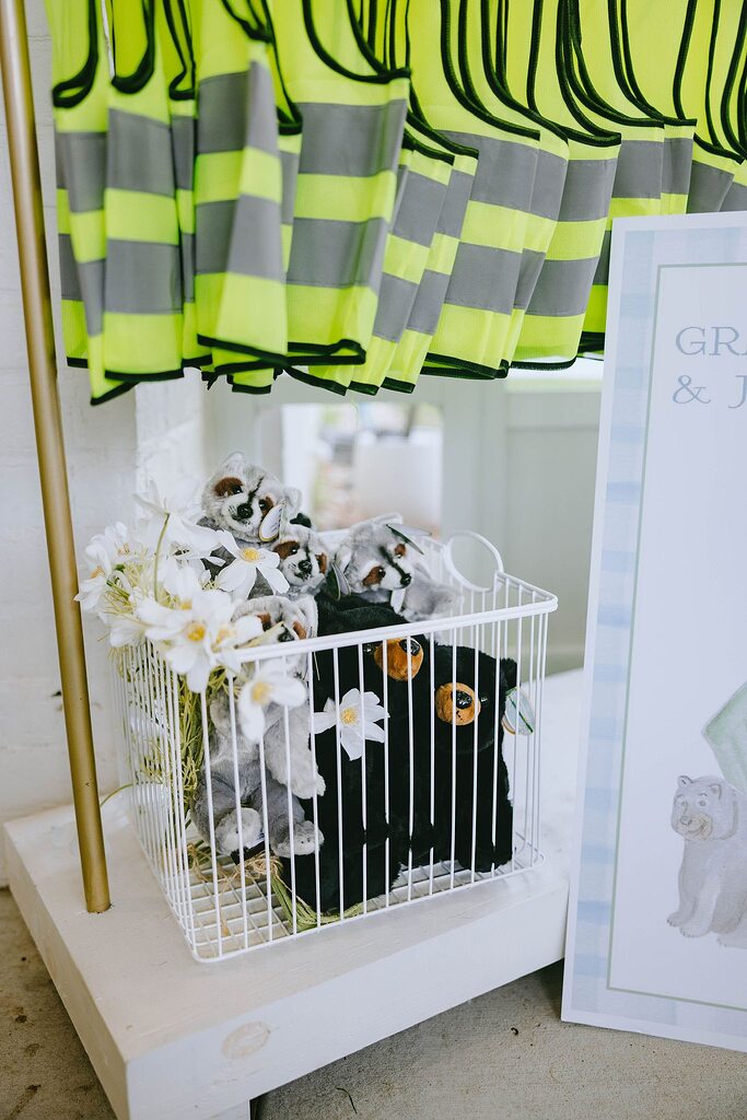 Plush raccoon and black bear toys in a white wire basket with white flowers.