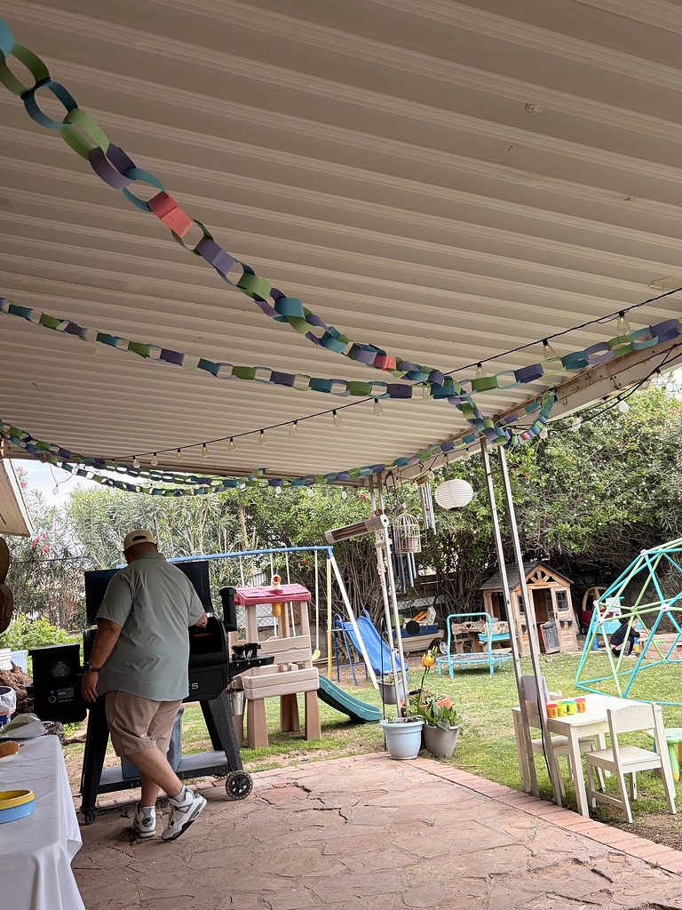 Man standing at a backyard grill under a patio cover decorated with paper chains