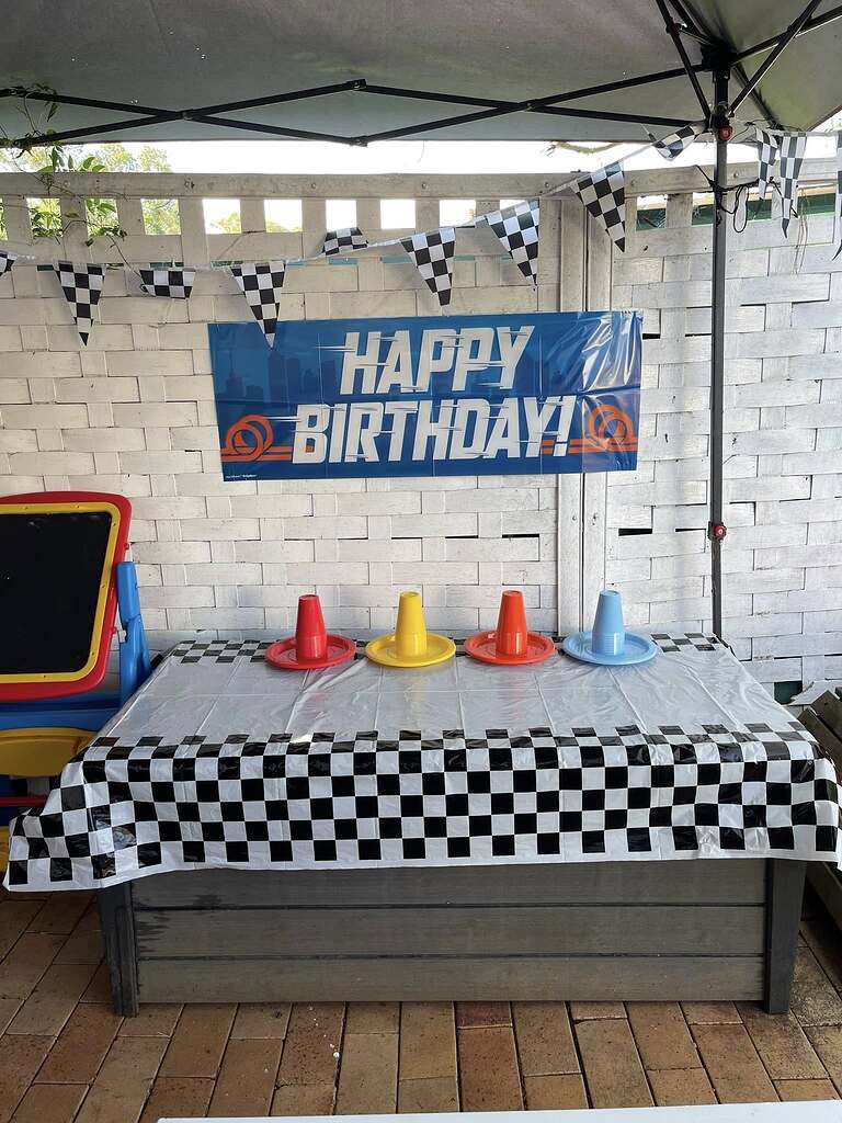 Race car-themed birthday table decorated with a checkered tablecloth, Happy Birthday banner, and colorful party cups.