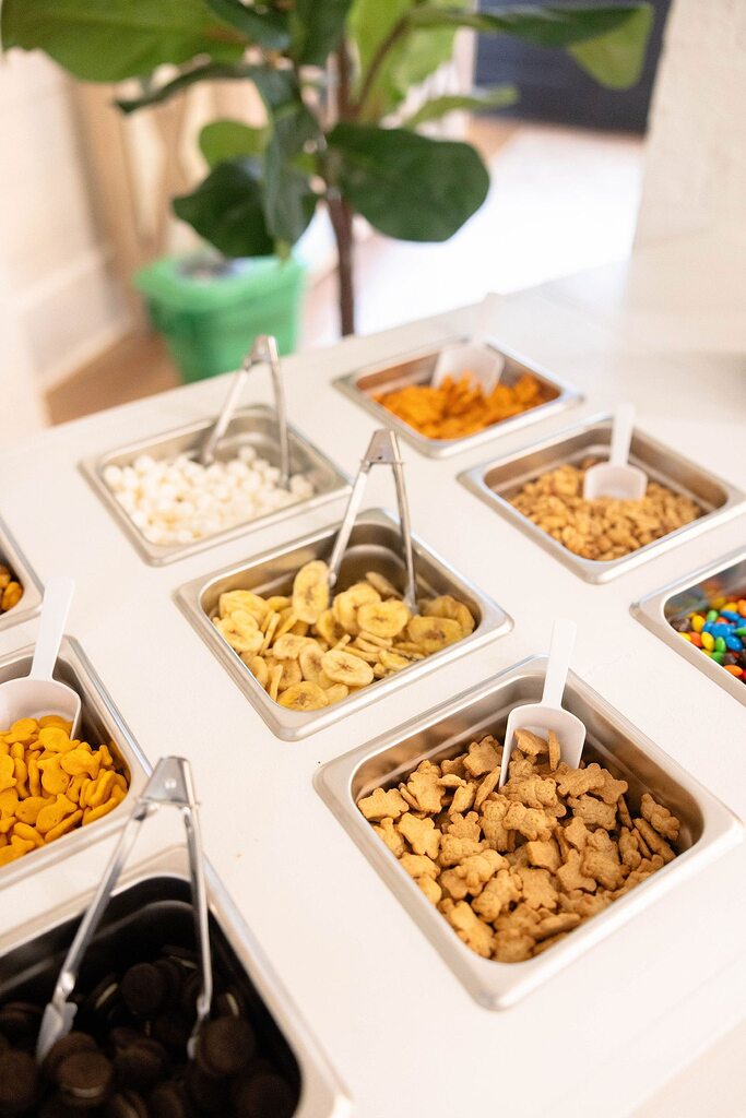 Snack bar setup with metal containers filled with varied treats like crackers, dried fruit, cookies, and candy.