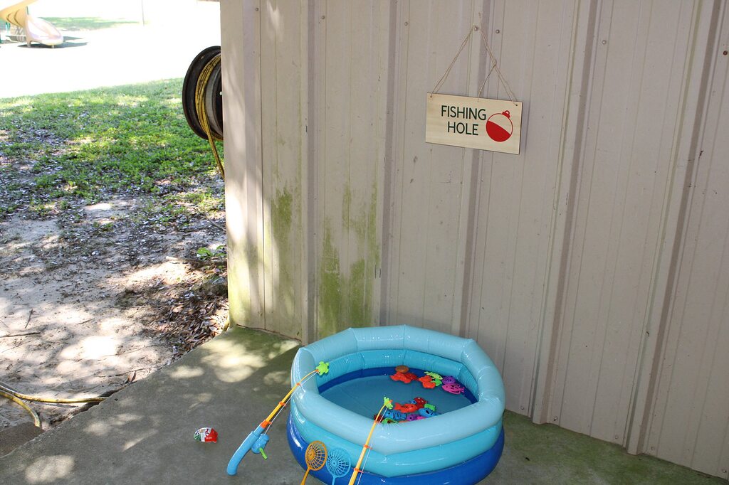Small blue inflatable kids pool set up as a fishing game with plastic fish and rods.