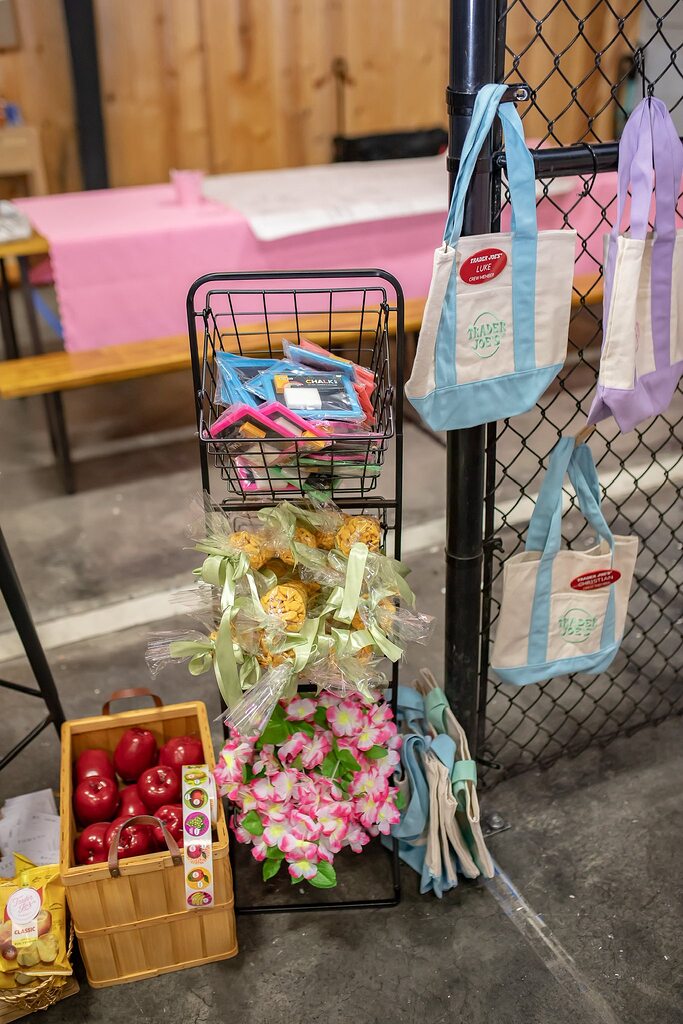 Display rack featuring bagged snacks, pastel canvas Trader Joe's tote bags, and a basket of fresh red apples.