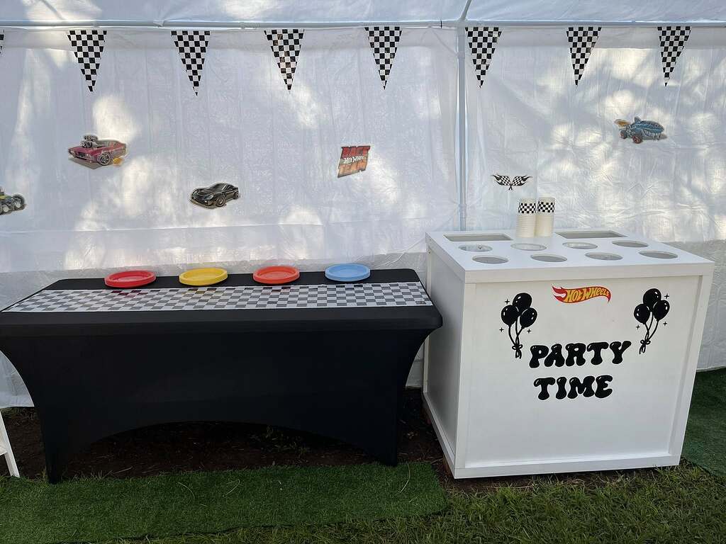 Hot Wheels themed party setup with checkered flag banners, race car wall cutouts, and a Party Time snack station.