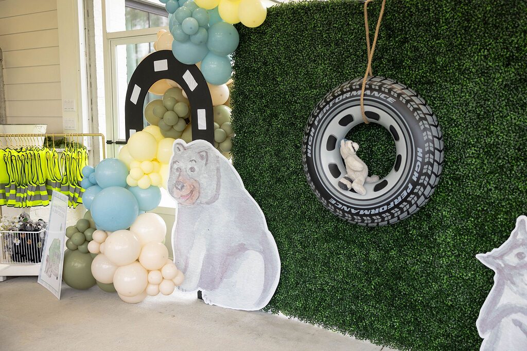 Bear themed birthday party backdrop with a balloon arch, hanging tire prop, and bear cutout.