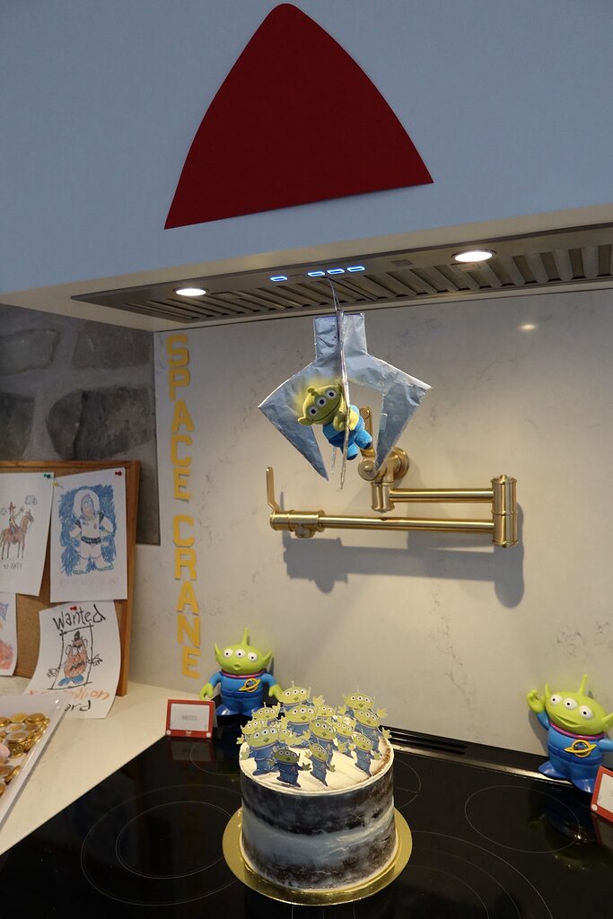 Toy Story inspired kitchen counter decor featuring a cake, alien figurines, and a DIY space crane hanging toy.