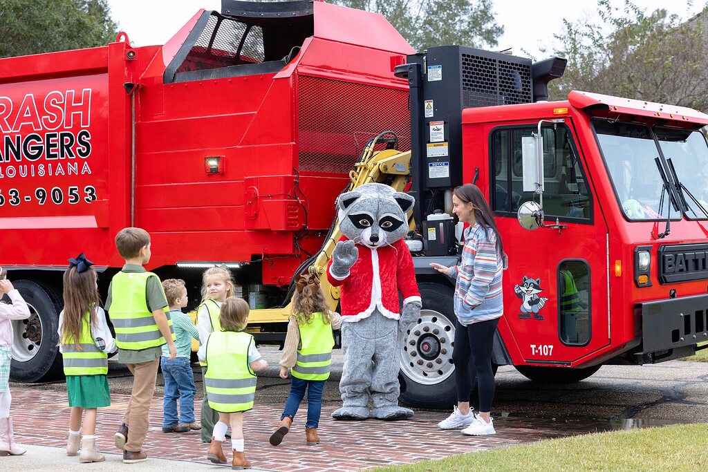 Trash Rangers mascot in a red jacket interacting with toddlers wearing safety vests by a red garbage truck