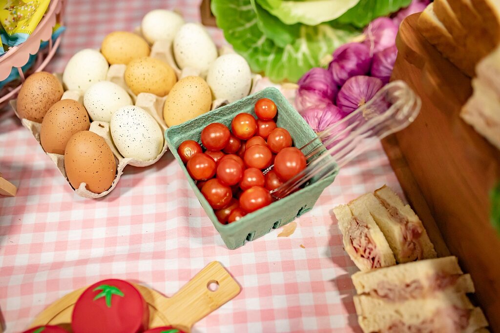 Table spread features a carton of fresh eggs, a basket of cherry tomatoes, red onions, and tea sandwiches.