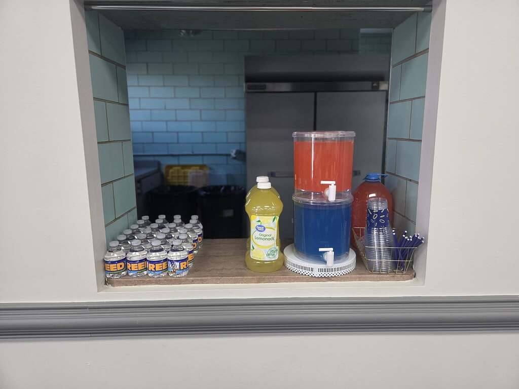 Drinks station with bottled water, lemonade, beverage dispensers, and stackable cups.