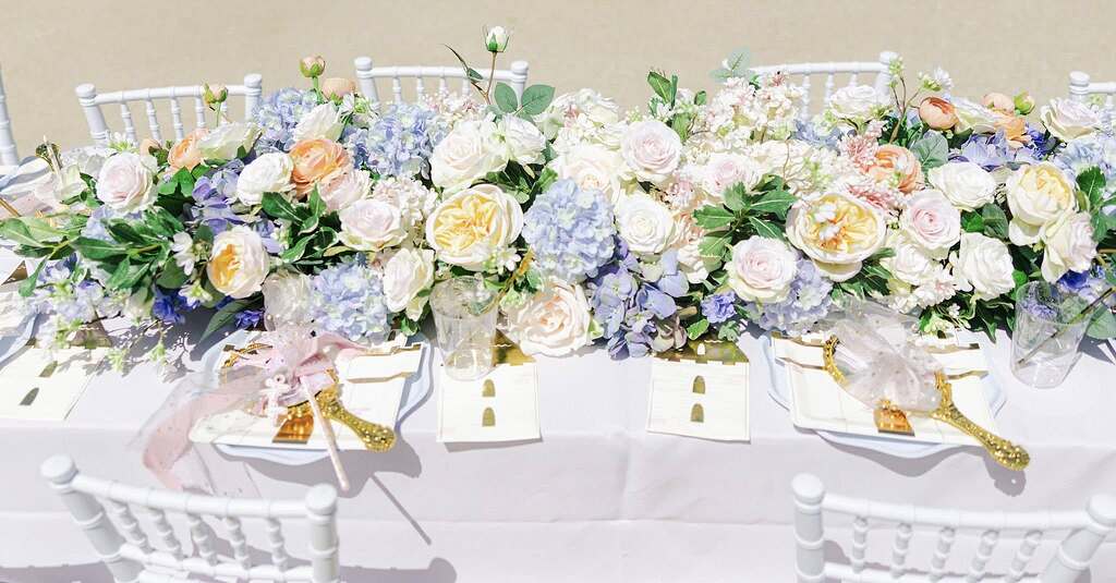Dining table decorated with an elaborate floral runner of pastel roses and blue hydrangeas for an event