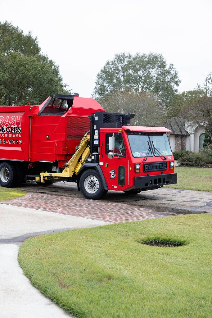 Bright red Trash Rangers garbage truck driving on a residential driveway.