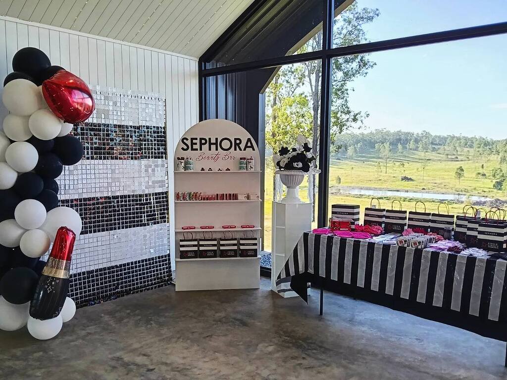 Sephora Beauty Bar setup with balloon arch, branded display shelf, and table of gift bags at an event.