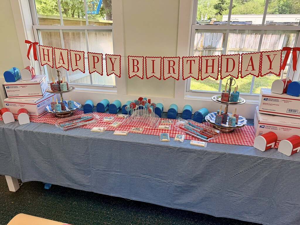 Mail-themed birthday party dessert table with Happy Birthday banner, miniature mailboxes, and red, white, and blue treats.