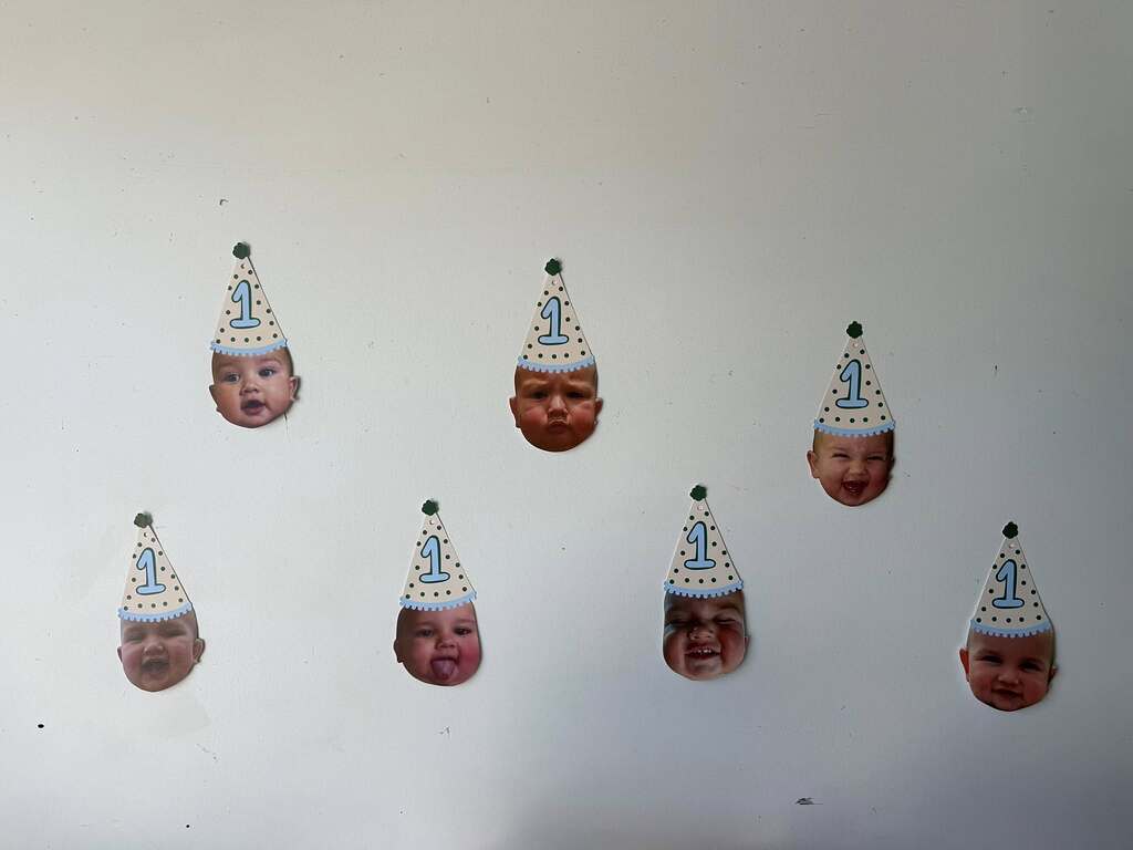 Seven custom cutouts of a baby's face wearing a blue polka-dot party hat with the number 1 for a first birthday