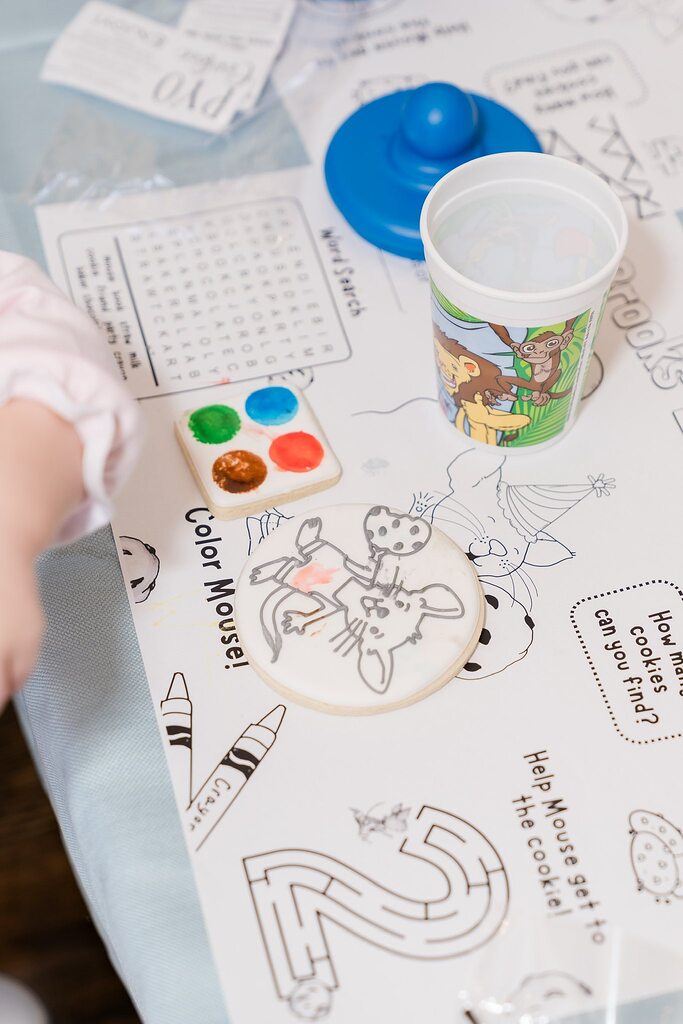 Decorated cookie, paint palette cookie, and water cup on activity placemat for Paint Your Own cookie kit.