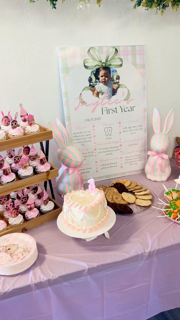 First birthday party table display featuring a themed sign, heart-shaped smash cake, cupcakes, and bunny decor.