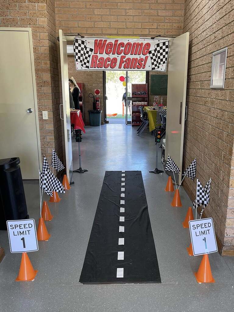 Race car themed party entrance with a Welcome Race Fans banner, road runway, cones, and speed limit signs.