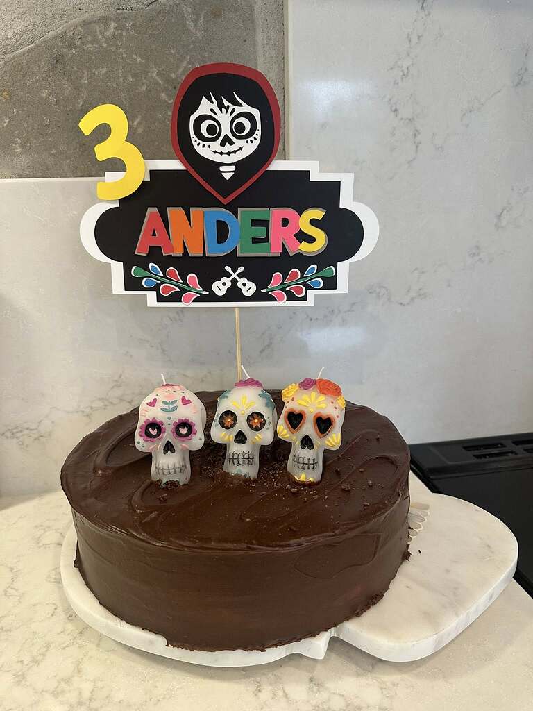 Chocolate cake decorated with a personalized Anders cake topper and three sugar skull candles for a 3rd birthday.