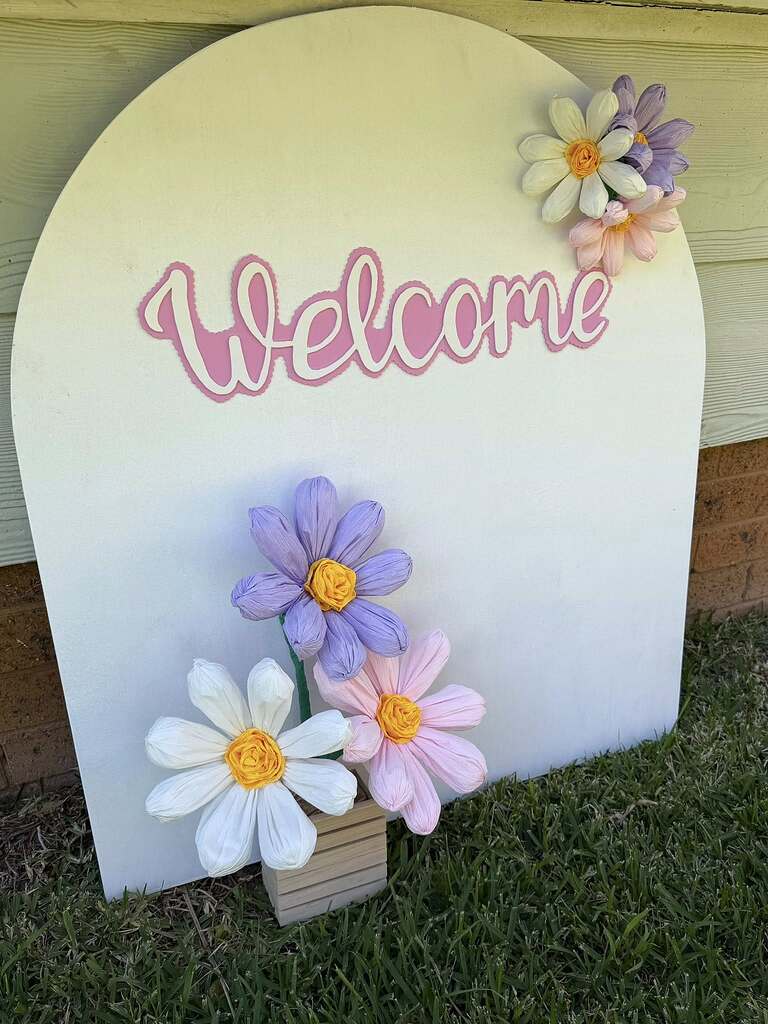Arched wooden welcome sign decorated with pastel paper flowers
