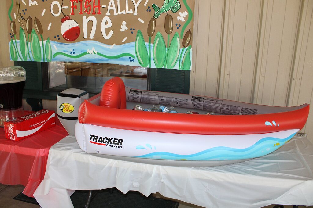Inflatable Tracker boat serving as a beverage cooler on a party table with 'O-Fish-Ally One' backdrop.