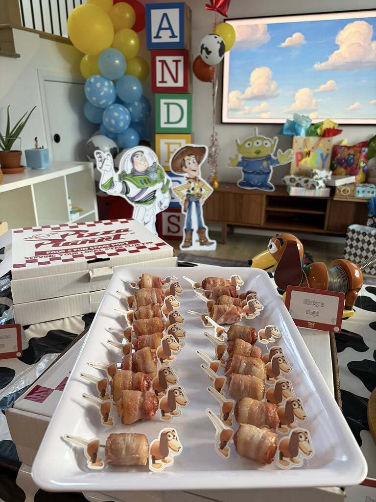 Bacon-wrapped pig in a blanket appetizers decorated with Slinky Dog themed party picks.