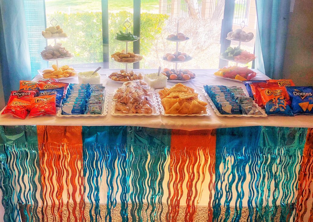Party snack table decorated with orange and blue fringe, featuring tiered serving platters and various snacks.