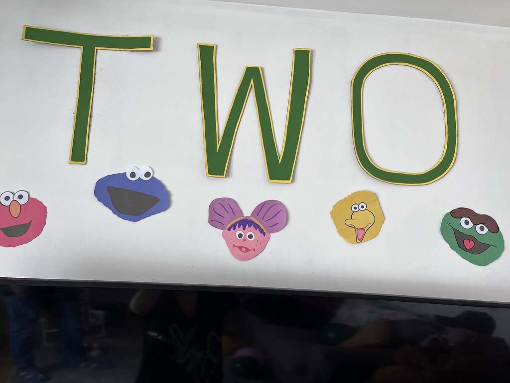 Wall decoration with the word TWO in green letters, themed with Sesame Street character cutouts.