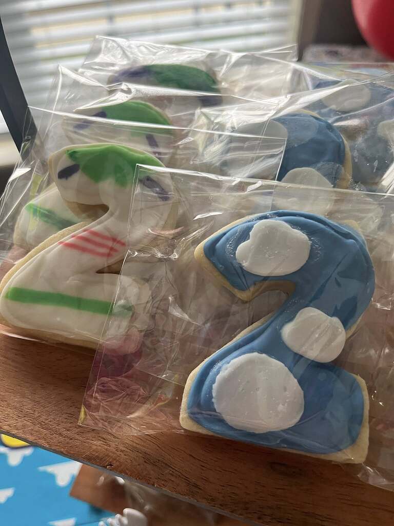 Individually wrapped sugar cookies shaped like the number two, decorated with white, blue, and green icing.