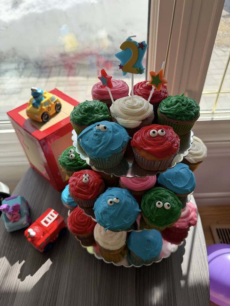 Tiers of colorful cupcakes decorated into monsters with candy eyes for a second birthday party.
